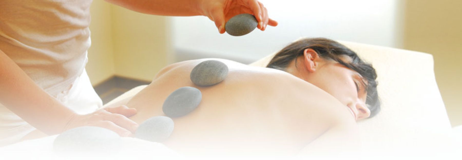 Hot-Stone-Massage: warme Steine werden auf den Rücken einer Patientin gelegt